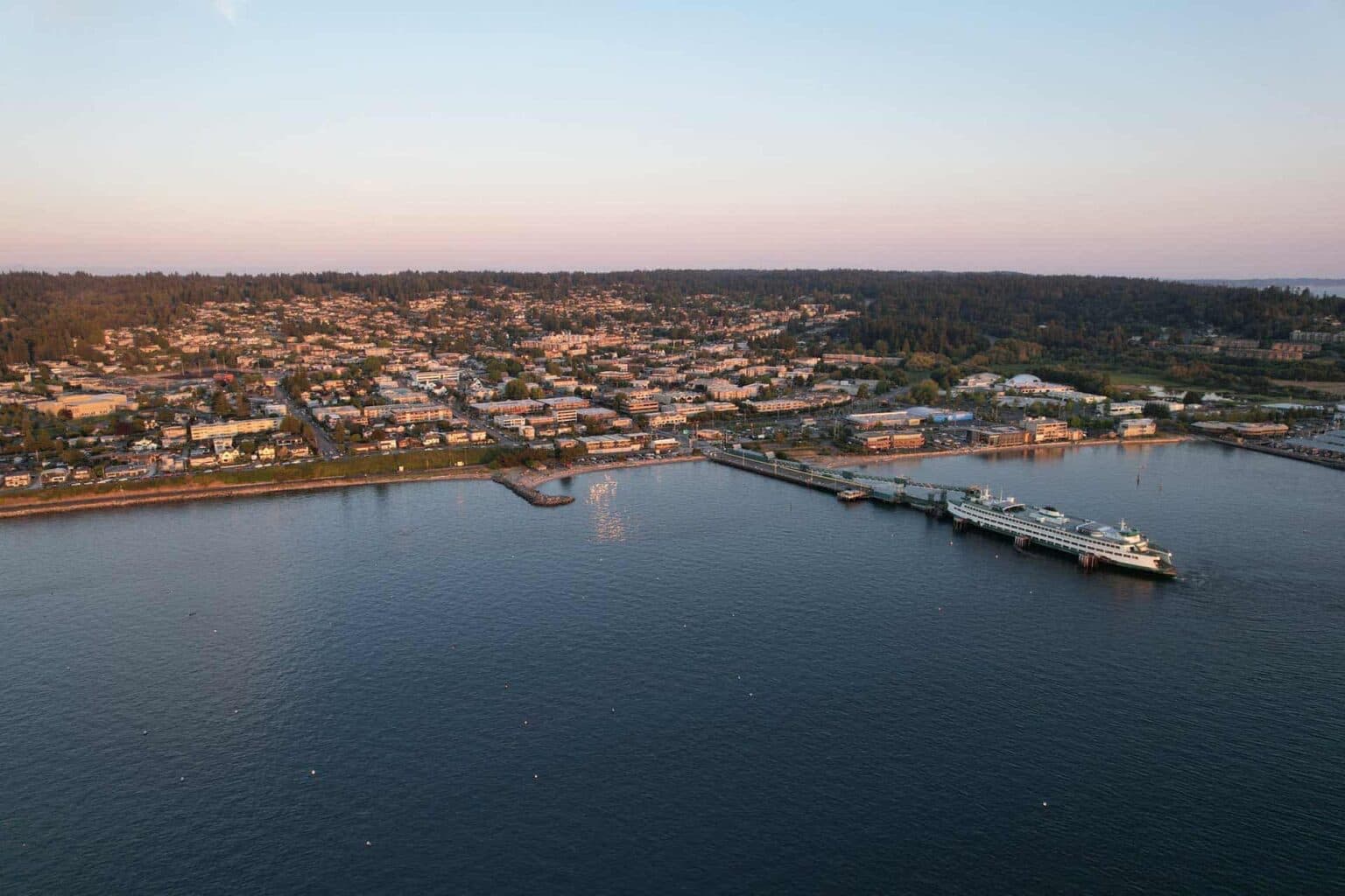 Aerial view of Edmonds, Washington, showing a mix of forested areas, suburban neighborhoods, and roads with Mount Rainier visible in the background under a clear blue sky.