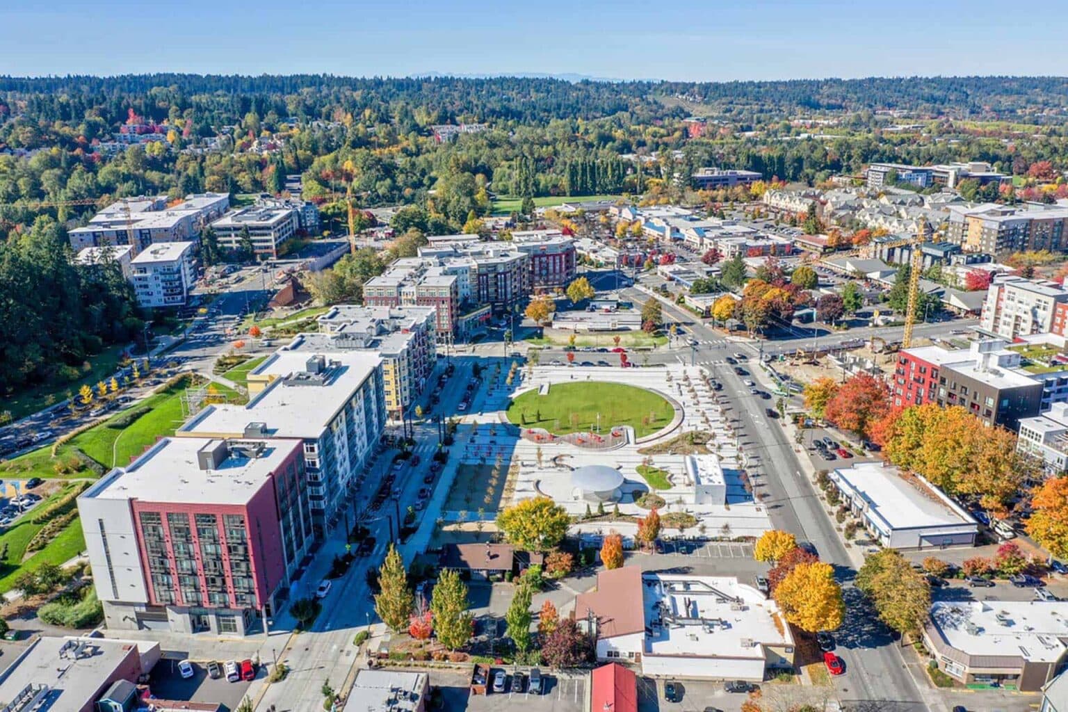 Aerial view of Redmond, Washington, showing a mix of forested areas, suburban neighborhoods, and roads with Mount Rainier visible in the background under a clear blue sky.