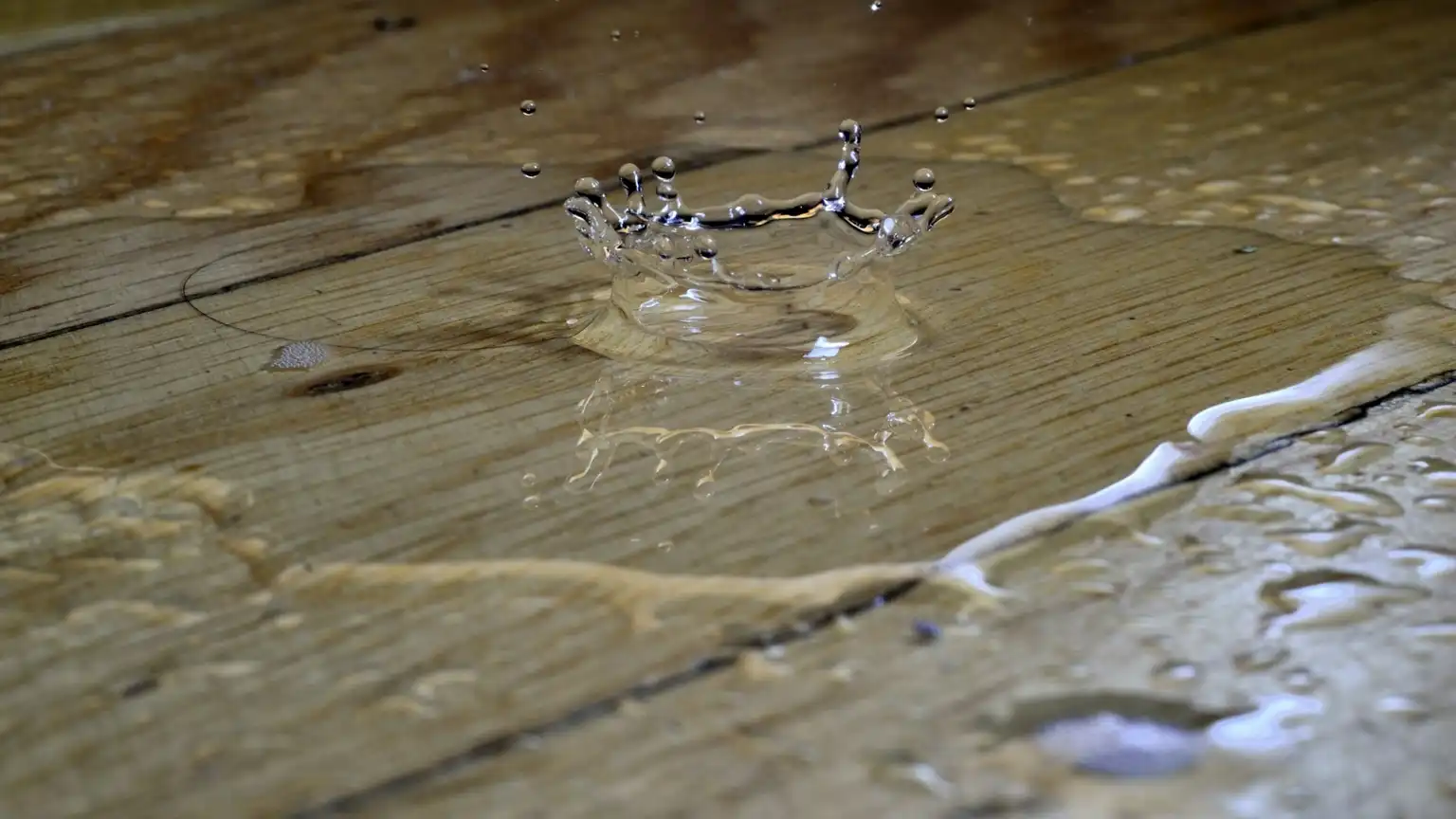 Close-up of water splashing on a hardwood floor, showing damage from a hidden leak in a home.