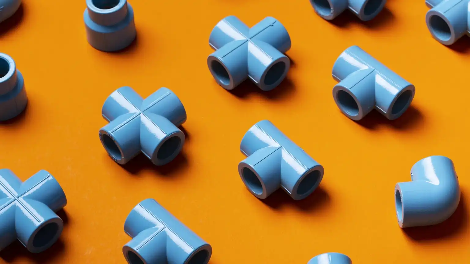 Assorted blue plastic pipe fittings, including T-joints, cross-joints, and elbow connectors, arranged neatly on a vibrant orange background.