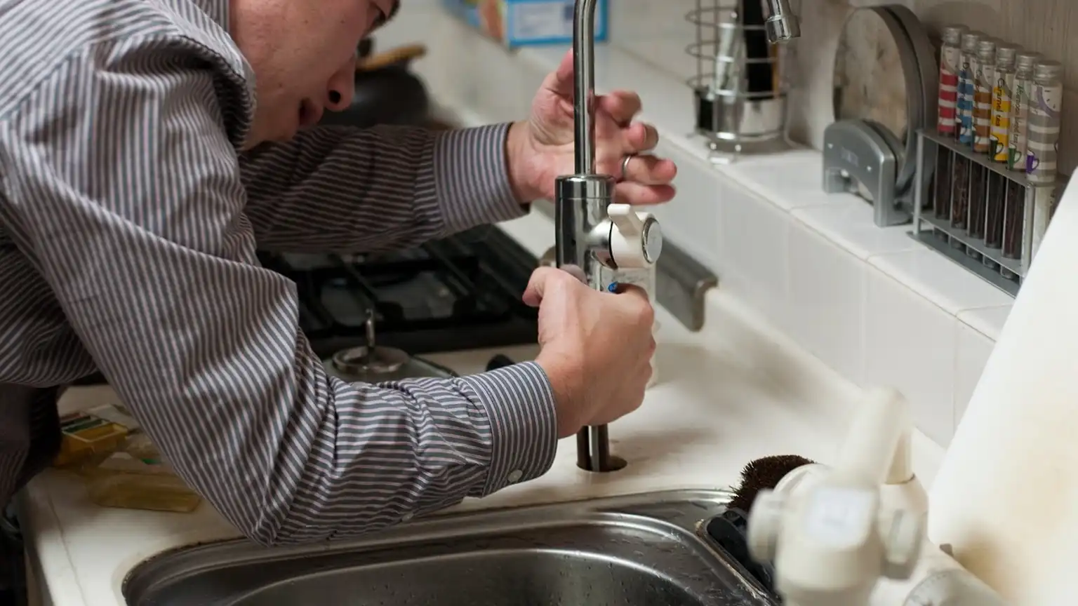 Plumber fixing a kitchen faucet to prevent water leaks.